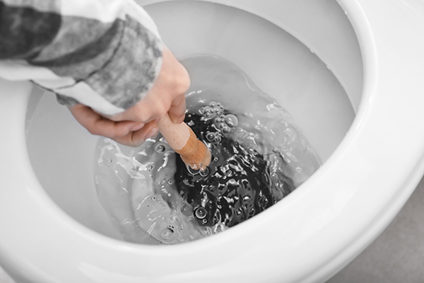 A hand holding a plunger inside of a toilet bowl