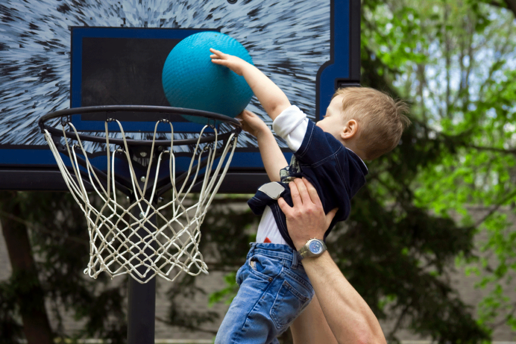 A small child being held up to slam dunk a basketball