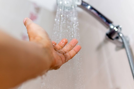 A hand feeling the water flowing from a shower head.